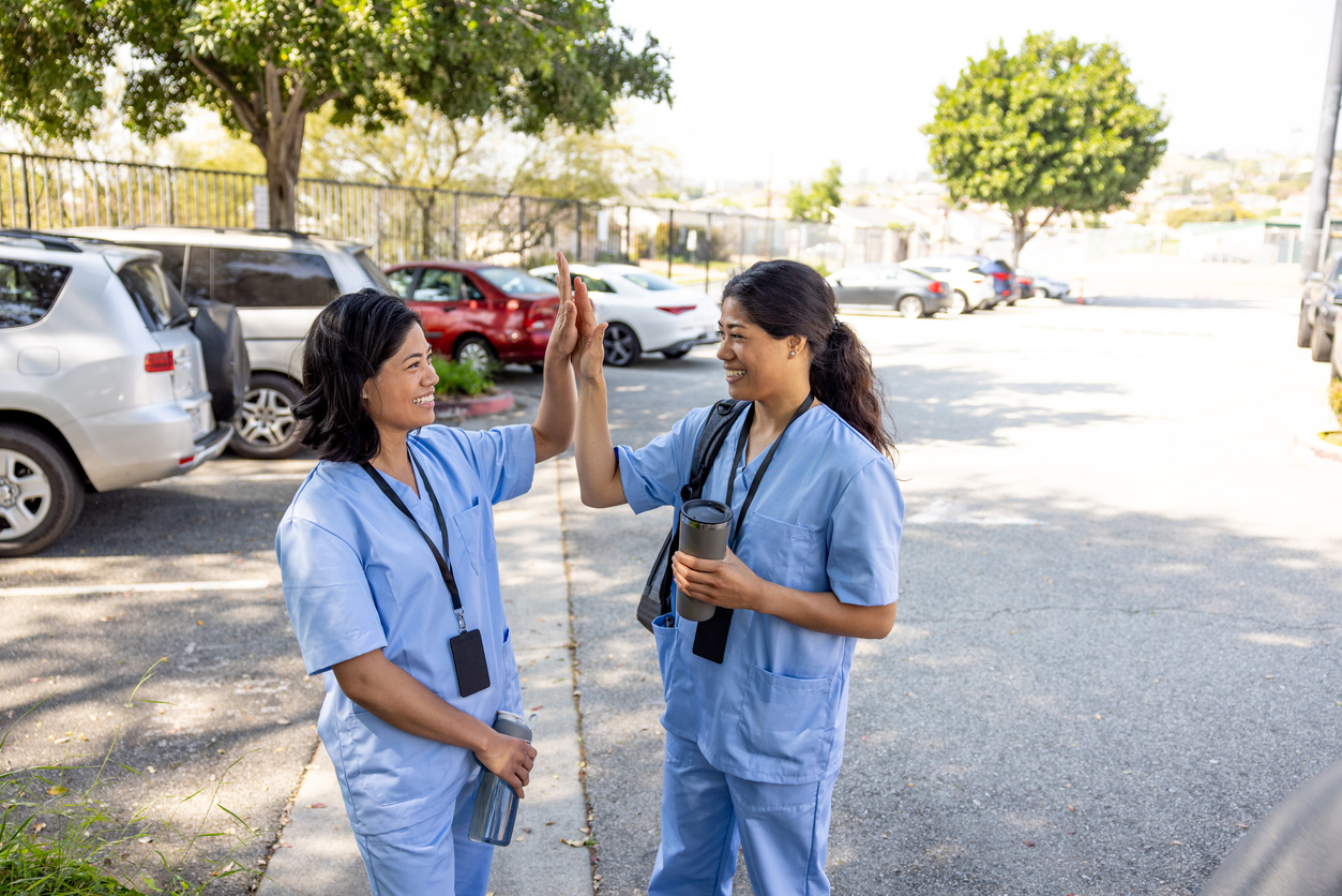 Two female hospital staff smiling and high fiving each other in the car park